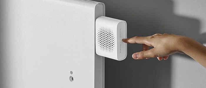 Une main dirig&eacute;e vers le diffuseur de parfum Thermor by Scentys branch&eacute; sur un radiateur